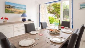 Un coin repas avec une table en bois dressée pour quatre personnes, des chaises, une lampe et un tableau accroché au mur.