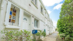 Une rangée de bâtiments blancs, séparés par une étroite ruelle, le tout entouré de verdure et sous un ciel dégagé.