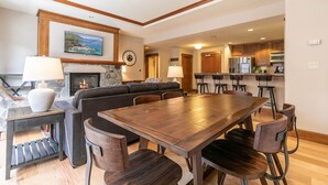 A spacious living room with a large wooden dining table, dark sofas, and a fireplace. - Iron Horse Lodge North 206 - delightful slopeside (Truckee)