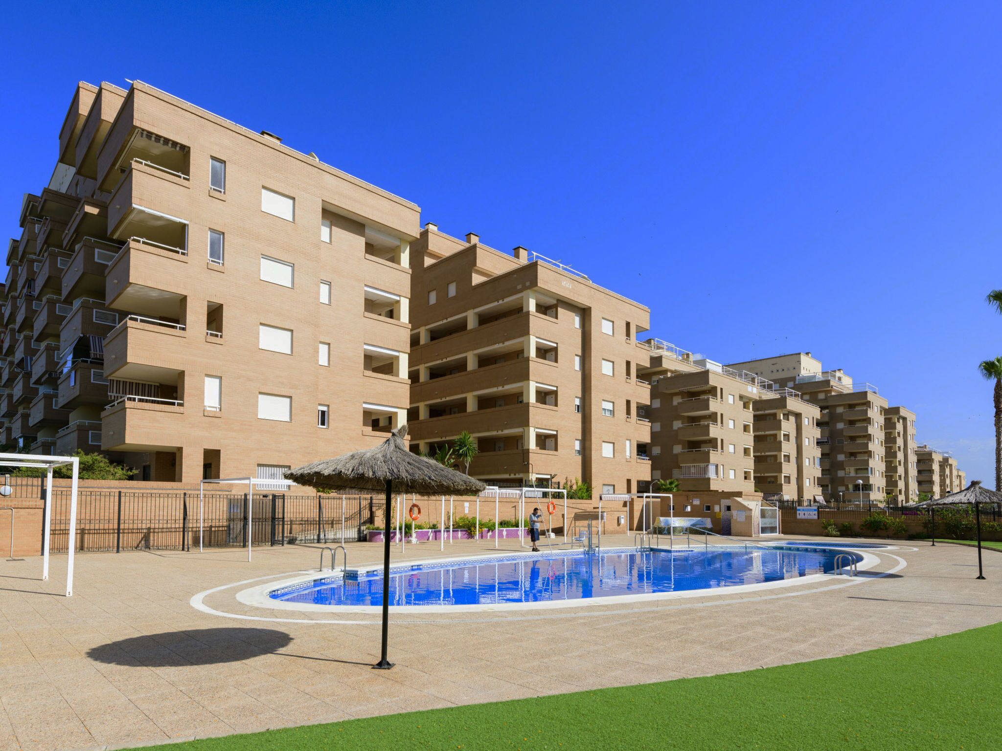 Un edificio residencial de varios pisos con balcones, piscina y zona verde.