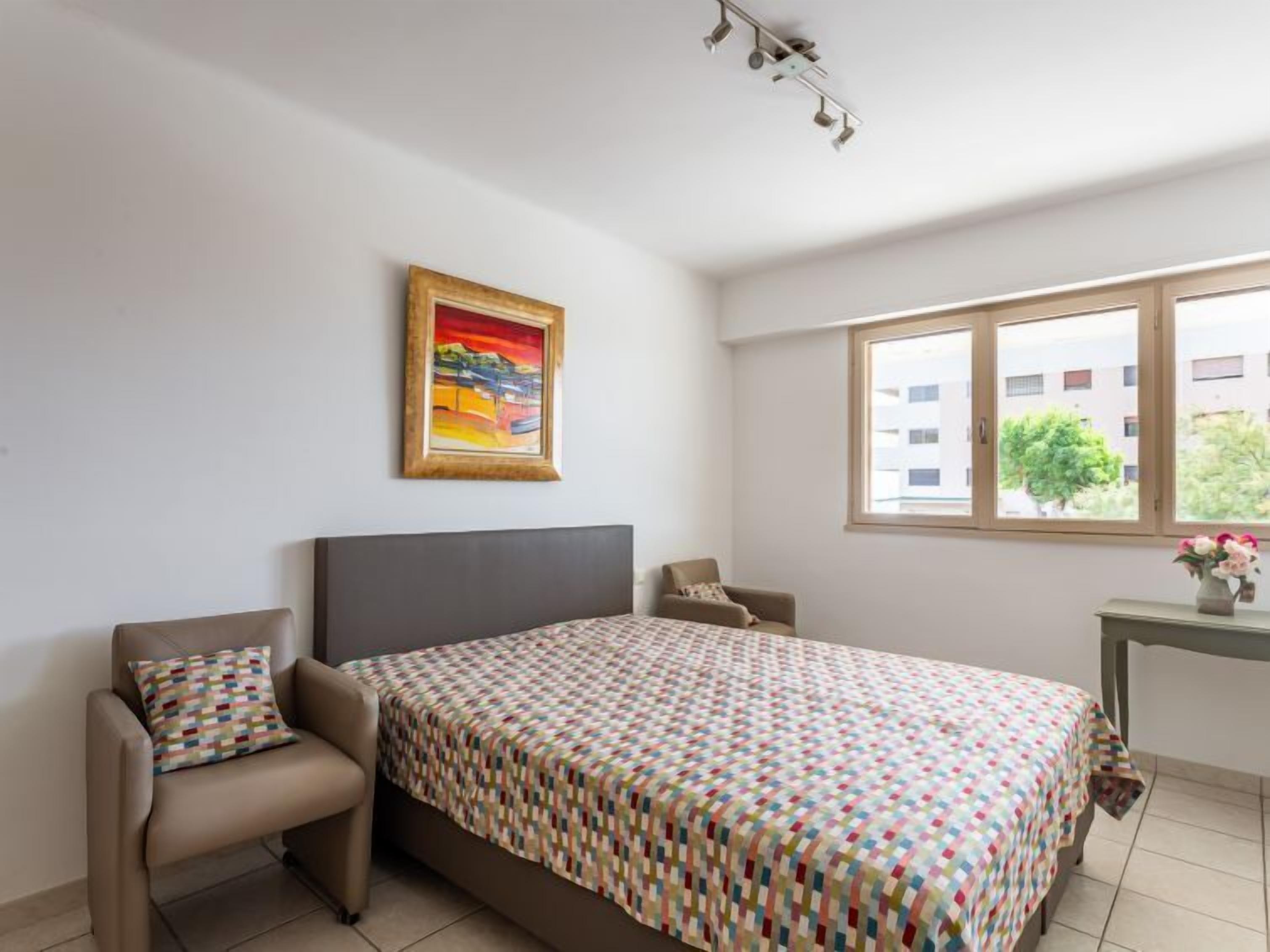 Una camera da letto con un letto, due sedie, una scrivania, una finestra e un quadro appeso al muro.