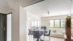 Un'area pranzo moderna con un tavolo rotondo e sedie, un divano bianco e un'ampia finestra con vista sul verde.
