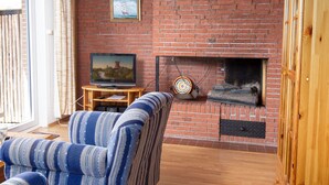 Een gezellige woonkamer met een met baksteen beklede open haard, een televisie en een gestreepte fauteuil.
