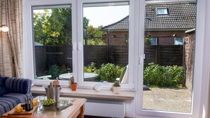Een kamer met een grote schuifdeur naar een tuin, een houten tafel met een afstandsbediening en een blauw gestreepte bank.