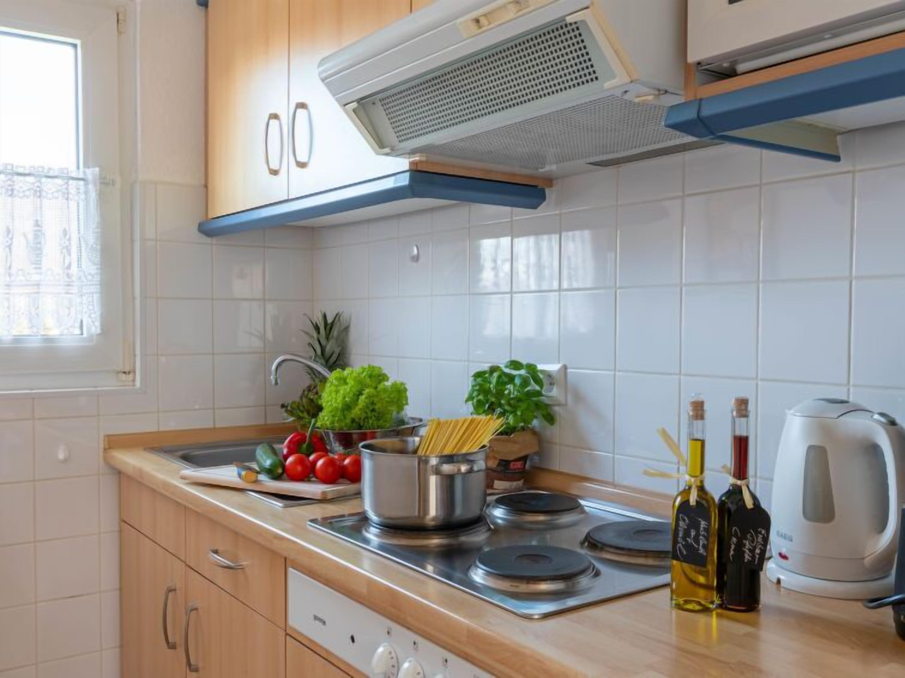 A modern kitchen with white tiles, wooden cabinets, a stainless steel stove, and a coffee maker.