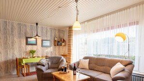 Ein gemütliches Wohnzimmer mit Holzbalkendecke, einer Couch, einem Esstisch und einem Bücherregal.
