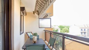 A balcony with a table, chairs, a potted plant, and a framed picture. - Saint James by Interhome (Le Lavandou)