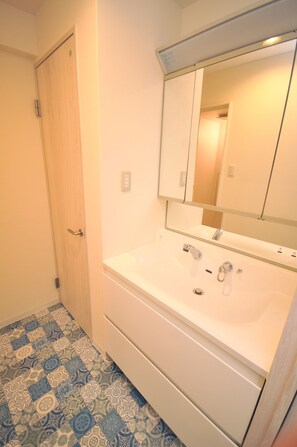 Un baño con lavamanos blanco, espejo y baldosas de suelo estampadas.