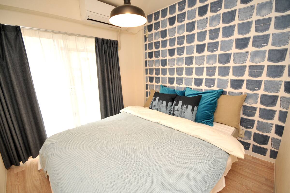 Un dormitorio con cama, cortinas, una pared con estampado vaquero y una lámpara de techo.