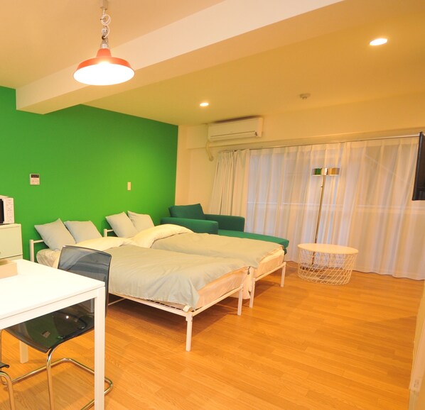 Una habitación con dos camas, un escritorio, una silla, una mesita y una cesta.