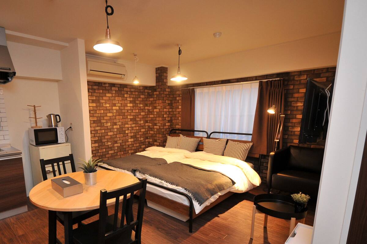 Habitación de hotel compacta con kitchenette, una cama y pared de ladrillo decorativa, además de un pequeño comedor.