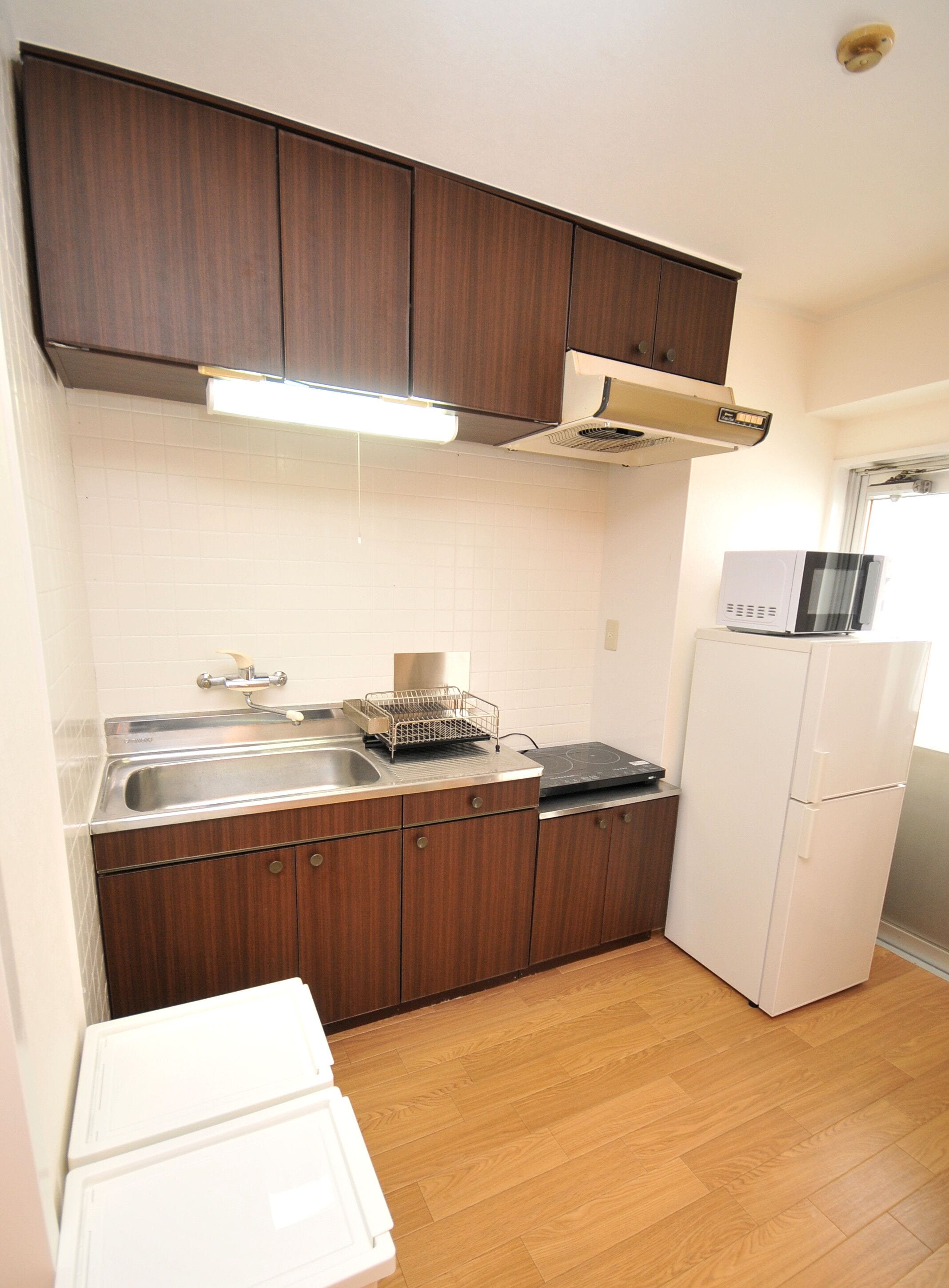 A compact kitchen with wooden cabinets, a stainless steel sink, a microwave, and a white refrigerator.