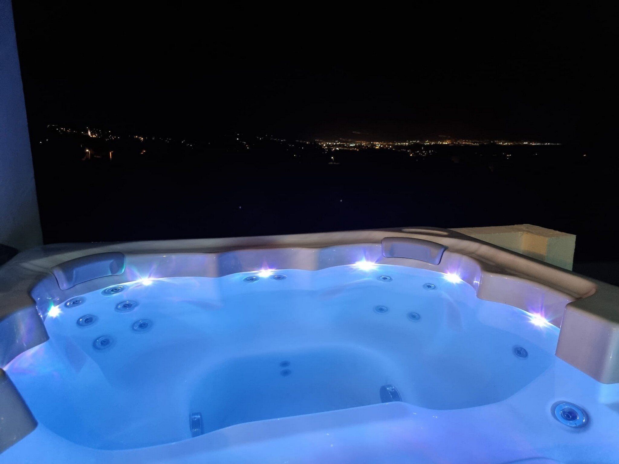 A hot tub with multiple jets, set against a night-time cityscape view.