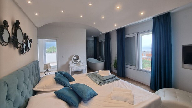 Un dormitorio moderno con una cama grande, una zona de estar, una bañera y vistas al exterior.