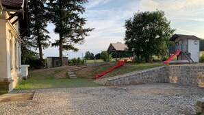 A playground with a red slide, a small pavilion, and a stone wall. - Spacious holiday home in Šluknov with private garden (Šluknov)