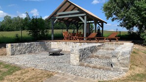 An outdoor patio with stone flooring, a grill, and wooden lounge chairs under a pergola. - Spacious holiday home in Šluknov with private garden (Šluknov)