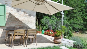A patio with a table and chairs under a large umbrella, a brick wall, and potted plants.