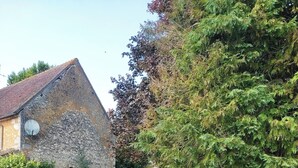 A stone building with a sloped roof, surrounded by lush greenery and flowering plants. - Village property in the Perche region with basic shops and SNCF train station. (Sablons sur huisne)
