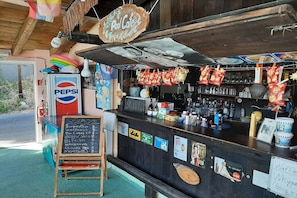 Un café junto a la piscina con una pizarra mostrando los alimentos, un refrigerador de Pepsi y diversos aperitivos colgados sobre el mostrador.