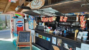 Un café situé au bord de la piscine, avec un réfrigérateur rempli de Pepsi, des sachets de collations et un tableau noir affichant le menu.