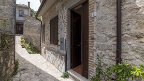 A narrow stone-paved alley with a rustic building featuring a wooden door and shutters.