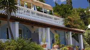 A two-story building with a balcony, potted plants, and a clear blue sky.