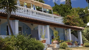 A two-story building with a balcony, potted plants, and a clear blue sky.