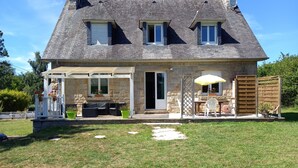 A two-story stone house with a covered patio, outdoor seating, and a wooden fence.