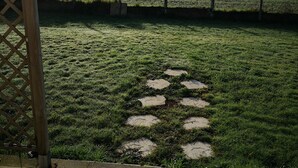 A paved area with a stone pattern, a wooden fence, and a grassy field with trees in the background.