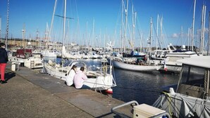 A marina with multiple boats docked, a woman sitting on a boat, and a man standing nearby.