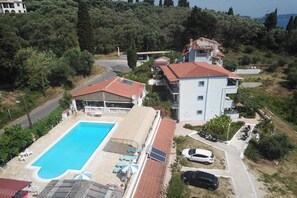 A residential property with a swimming pool, multiple buildings, and parked cars. - Apartment in Mpenitses with Sea Views & Pool (Mpenitses)