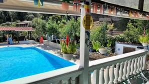 Zona de piscina con piscina azul cristalina, barandilla blanca y plantas en macetas.