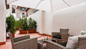 Un patio con mobiliario de mimbre, plantas en macetas y un paraguas grande.