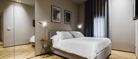 A modern bedroom with a large bed, a mirror, two wall-mounted lights, and a window with curtains.