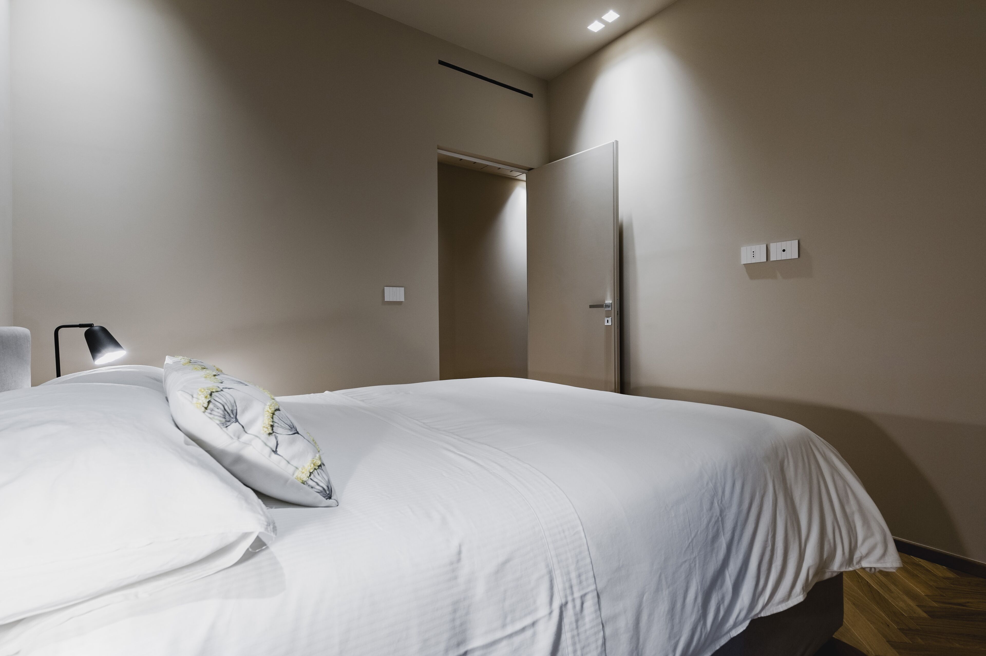 A bedroom with a bed, a nightstand, a lamp, and a door.