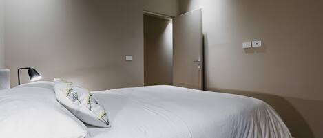 A bedroom with a bed, a nightstand, a lamp, and a door.
