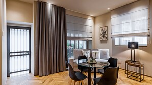 Una sala de estar moderna con una mesa de comedor de cristal, sillas negras, un sofá y un ventanal con cortinas.