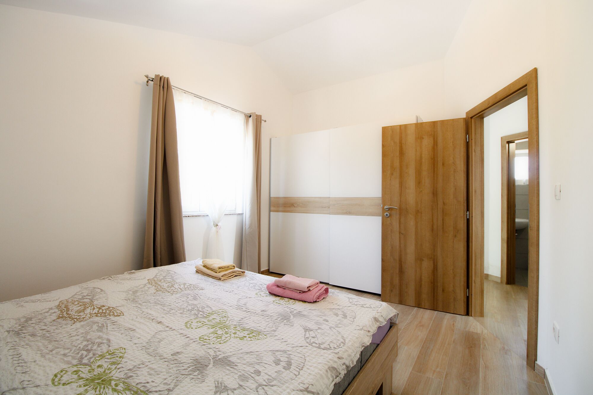 Een slaapkamer met een bed, een houten deur en een raam met gordijnen.