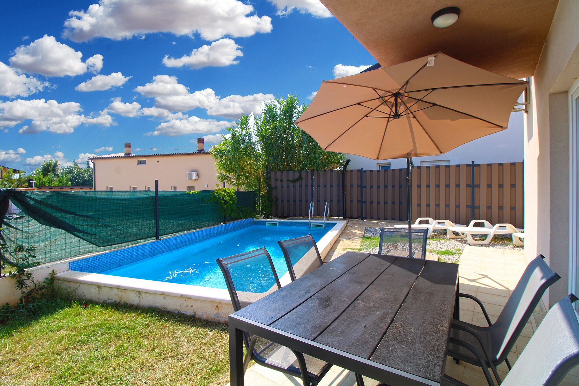 A backyard with a swimming pool, a table, chairs, and an umbrella.