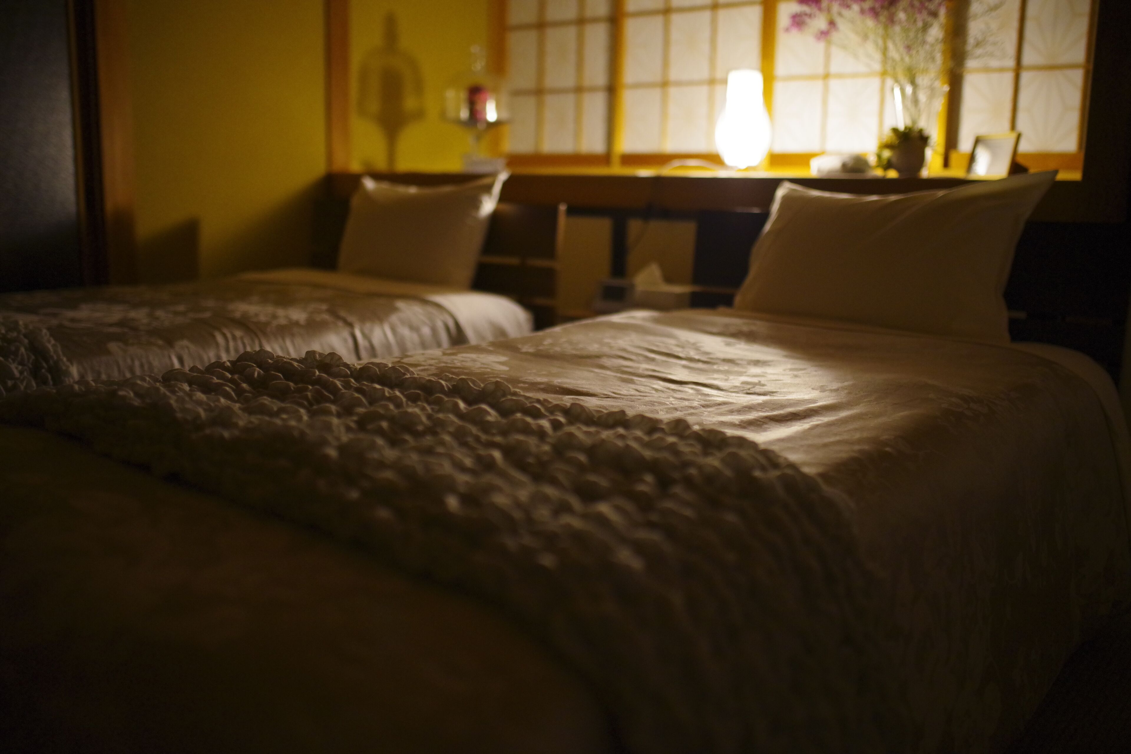 A dimly lit hotel room with two beds, a wooden headboard, and a window with a view of the outside.