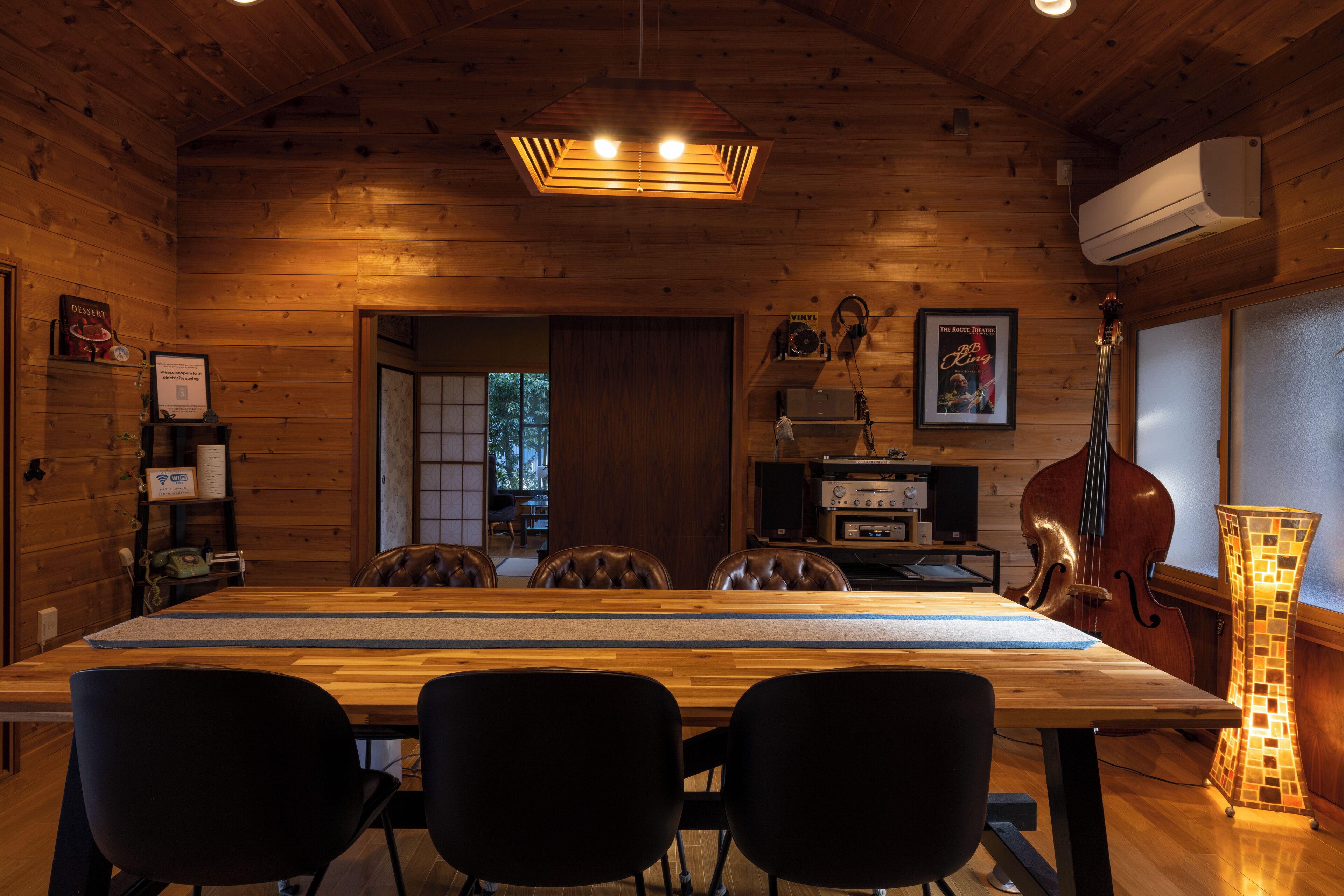 A wooden interior with a long dining table, black chairs, a cros