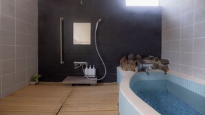 A modern bathroom with a wooden floor, a bathtub with blue tiles, a black wall, and a small window. - Azumino Salon (Azumino)