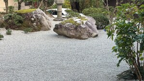 A garden with large rocks, a statue, and a building with a red roof. - Azumino Salon (Azumino)