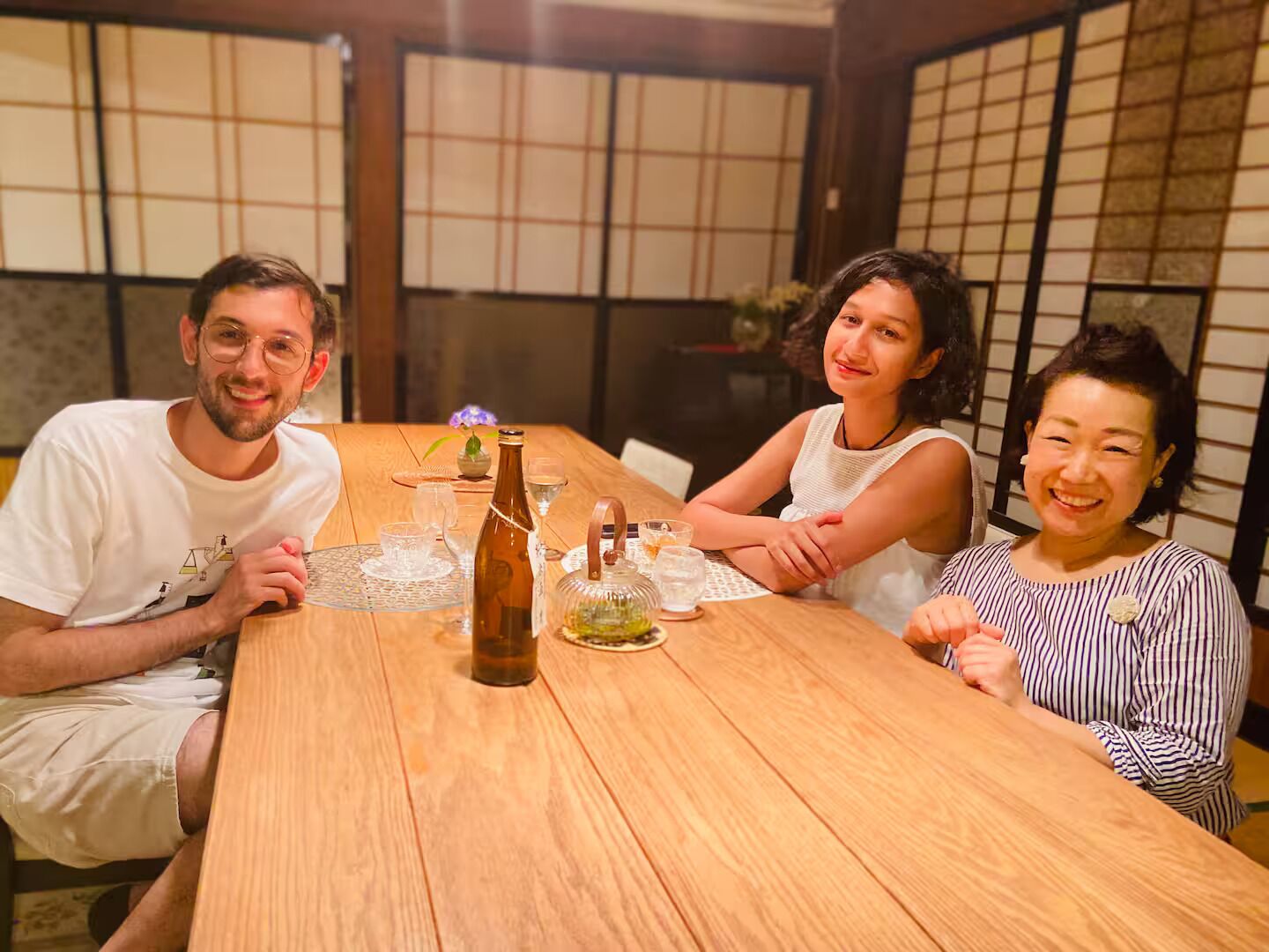 A wooden dining table with a bottle, glasses, and a small vase.