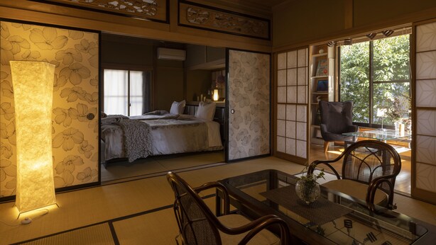 A traditional Japanese room with tatami flooring, a low table with chairs, a bed with a futon, and sliding doors with floral patterns. - Azumino Salon (Azumino)