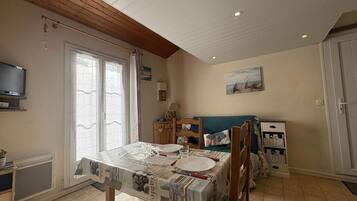 Un coin repas avec une table dressée pour deux personnes, un téléviseur fixé au mur et une nappe aux motifs évoquant la plage.