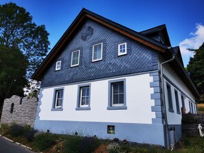 Uma casa de dois andares com telhado escuro de ardósia, paredes brancas e alicerce de pedra.