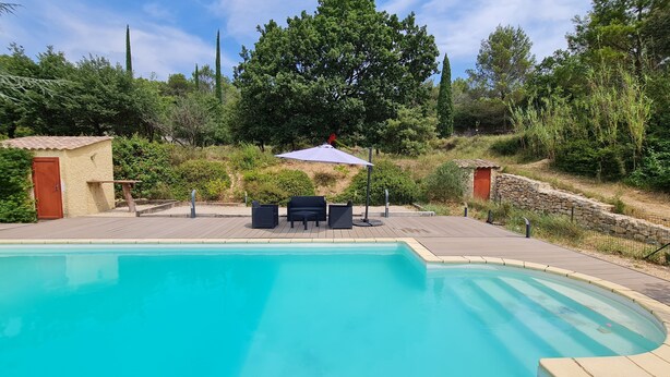 Une piscine avec une terrasse en bois, du mobilier d’extérieur et un mur en pierre.