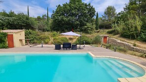 A swimming pool with a wooden deck, outdoor furniture, and a stone wall.