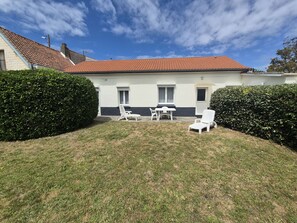 A house with a red-tiled roof, white exterior walls, and a small front yard with a lawn and two white chairs.